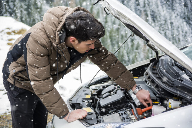 Man inspecting car engine in the snow