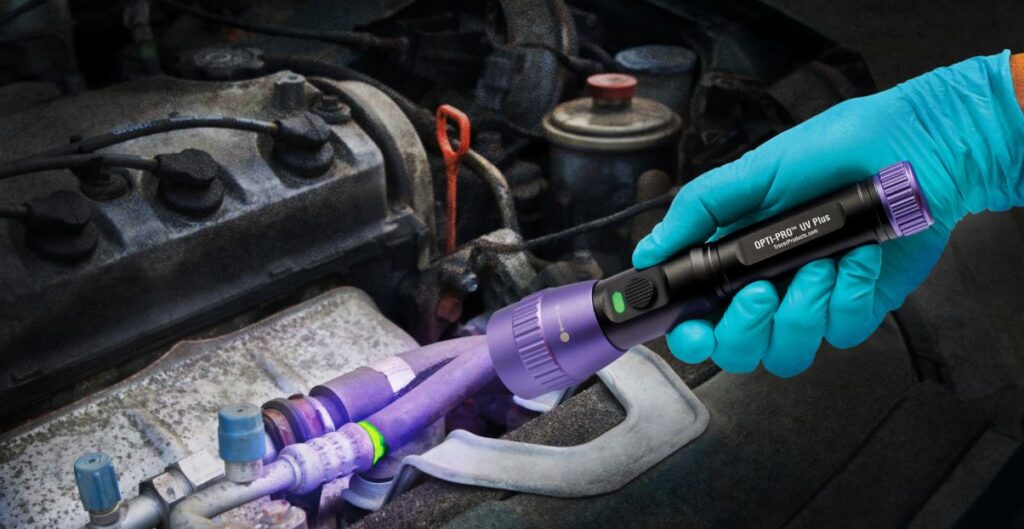 Technician using UV light to detect A/C refrigerant leak in hybrid vehicle
